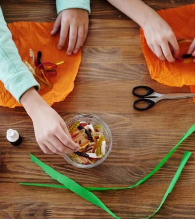 Two children preparing treats with candies and wrapping them creatively for Halloween festivities.